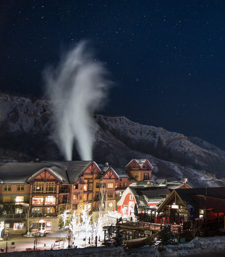 High Angle Shot Of A Beautiful Town With Wooden Buildings And Bright Lights On The Streets Surrounded By Scenic Winter Landscape